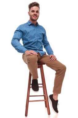 mavi bir gömlek giymiş çekici casual adam ahşap beyaz arka plan, tam vücut resim taburede oturur