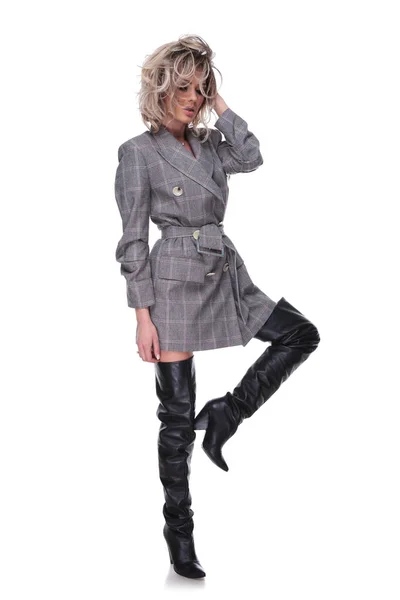 魅力的な女性が身に着けている灰色のスーツのジャケットと長い革ブーツ髪を固定し 全身画像下へ見ている中で上げられた脚ポーズ — ストック写真
