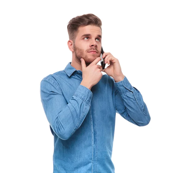 電話で話していると 白い背景の上に立っている間側を見上げる物思いにふけるのカジュアルな男性の肖像画 — ストック写真