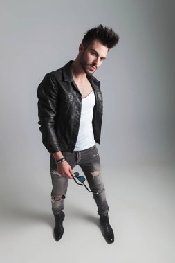 seksi genç erkek deri ceket ve kot duran güneş gözlüğü açık gri renkli, geniş açı resim üzerinde tutar.