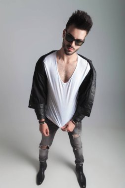 yakışıklı erkek deri ceket giymiş onun beyaz t-shirt dururken ışık gri arka plan üzerine çeker.