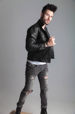 yakışıklı erkek deri ceketi tutarak açık gri renkli, tam vücut resim üzerinde tahta bir sandık üzerinde dururken yanına döner