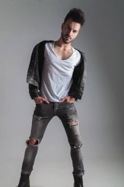 seksi erkek deri ceket ve gri kot pantolon üzerinde açık gri renkli elleri ceplerinde, baştan çıkarıcı, arıyorsunuz tam vücut resmi duruyor