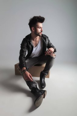 deri ceket ve Gri Jeans oturan adam tarafına ışık gri arka plan üzerinde görünüyor.