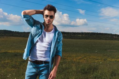 casual yakışıklı bir kot gömlek ve güneş gözlüğü takmış saçları dışında dururken bir çim alanda giderir.