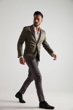 Yeşil elbiseli kendine güvenen erkek tarafına ışık gri arka plan üzerinde yürür ve geri, tam vücut resim görünüyor