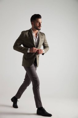 yakışıklı genç yeşil elbise düğmeler ve tarafına ışık gri arka plan üzerinde yürüyor