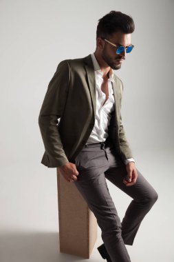 güneş gözlüğü ile çekici bir genç adam ahşap kutu üzerinde duruyor ve tarafına ışık gri arka plan üzerinde görünüyor