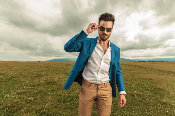 Attractive Man Suit Arranges His Sunglasses While Standing Grass Field — Stock Photo, Image