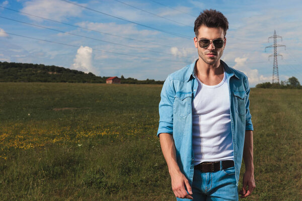 portrait of casual man with sunglasses standing on a field in the countryside, in daylight