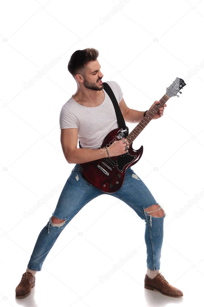 young star performing on an electric rock guitar while standing on white background, looking to side, full body picture