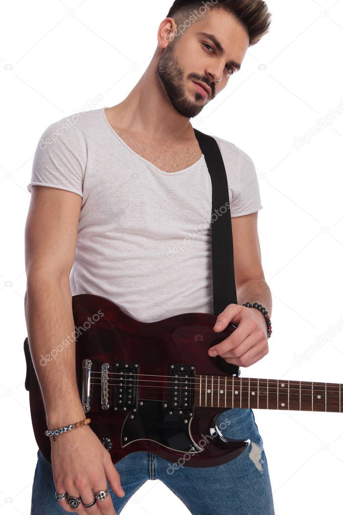 portrait of seductive young rockstar holding his electric guitar while standing on white background
