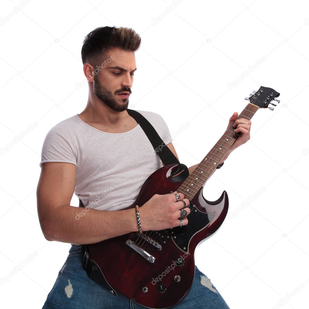 portrait of casual man strumming his electric guitar while standing on white background