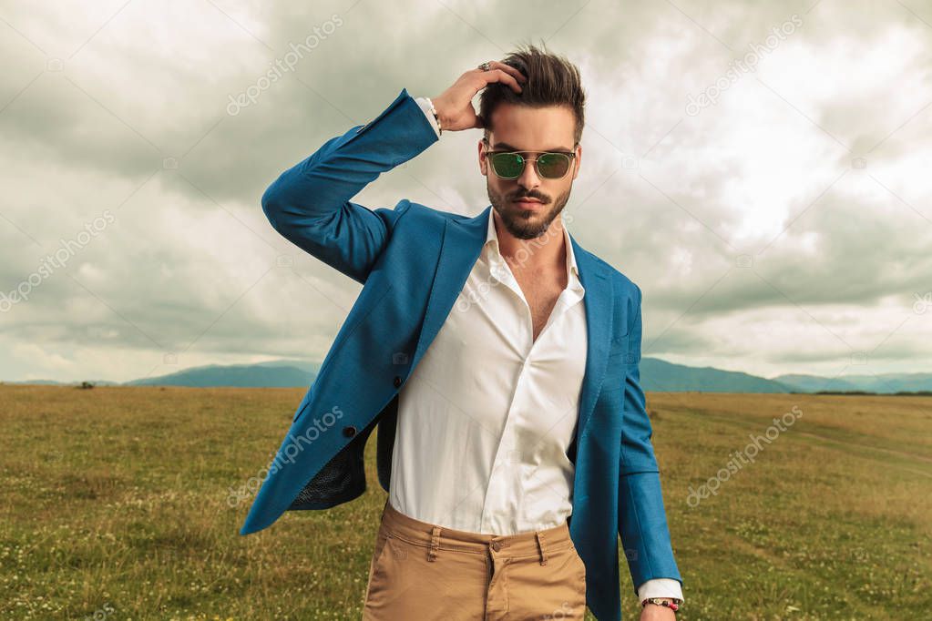 smart casual man with sunglasses fixing his hair in a grass field, portrait picture