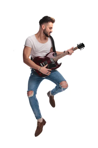 年轻的摇滚明星在演奏吉他的时候在白色背景的音乐会上跳跃 — 图库照片
