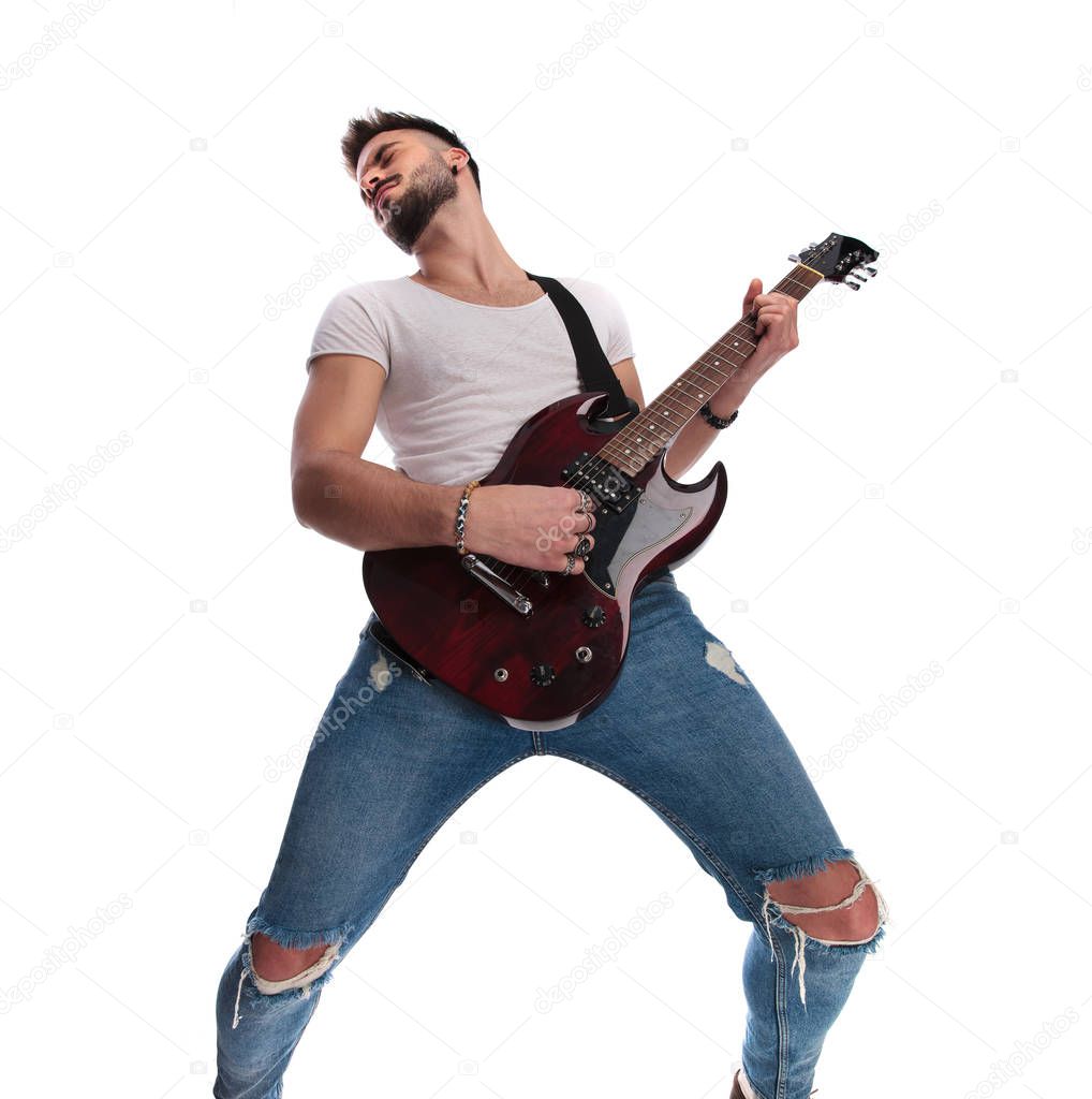 excited young guitarist playing the guitar  and leaning back while standing on white background