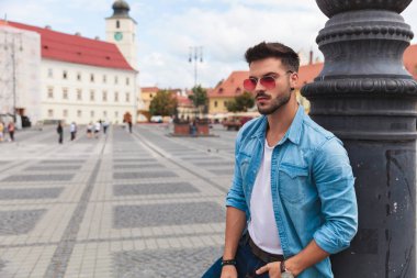 bir çift güneş gözlüğü ve bir kot mavi gömlek giyen genç casual adam yaya caddesi üzerinde duruyor ve tarafına, portre resim arıyor