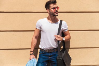 mavi gömleği ve omuz çantası turuncu bir duvarının yakınında dururken yan isteyen holding yakışıklı casual adam portresi