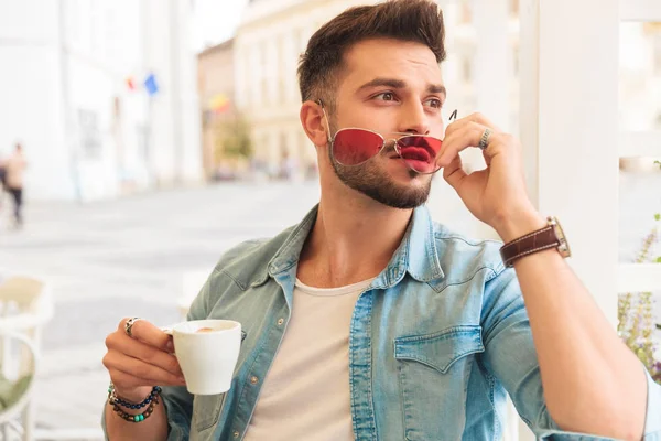 Zaskoczony Młodzieniec Picia Kawy Siedząc Odkryty Zdejmuje Okulary Wygląda Bok — Zdjęcie stockowe