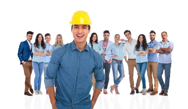 兴奋的临时小组组长的工程师与他的团队站在后面的白色背景 他戴着保护头盔 穿着蓝色衬衣 — 图库照片