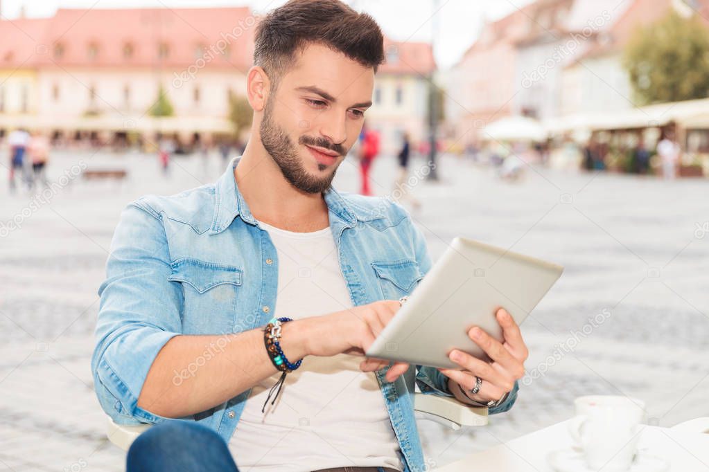 handsome casual man tapping his tablet while sitting in the city center, outside picture