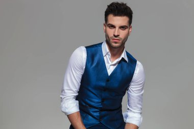 gri bir arka plan üzerinde portre resim otururken bir mavi yelek giymiş yakışıklı genç