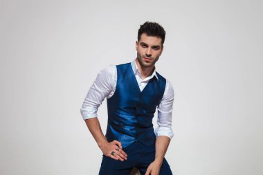 ışık gri arka plan üzerinde otururken bir mavi Jile giymiş yakışıklı genç adam portresi
