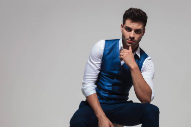 sakallı ışık gri arka plan üzerinde otururken bir mavi yelek düşünme giymiş seksi adam portresi
