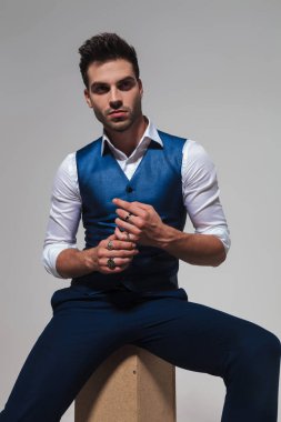 yakışıklı adam şık yelek ise ahşap sandık üzerinde oturan ve açık gri renkli, portre resim tarafına bakarak onun yüzük sabitleme