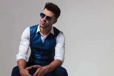 güneş gözlüğü ve ışık gri arka plan üzerinde rahatlatıcı ve tarafa bakarken yelek giyen şık adam
