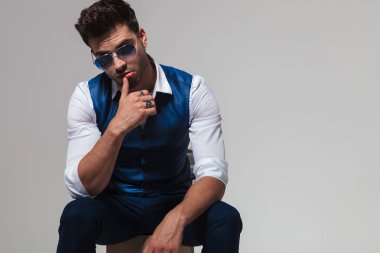 oturma ve açık gri renkli dudaklarından başparmak ile poz gözlüklü baştan çıkarıcı adam