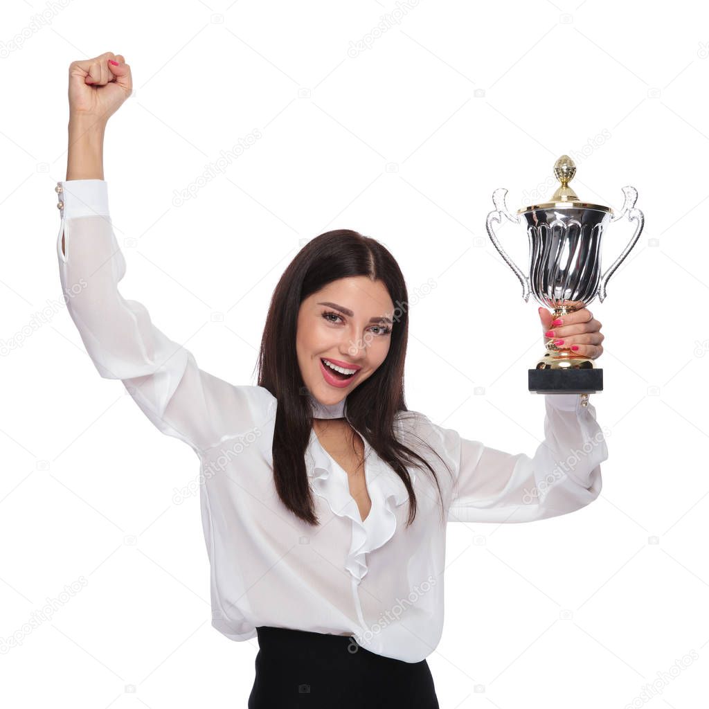 excited businesswoman holding the winning cup is celebrating with hand in the air while standing on white background, portrait picture
