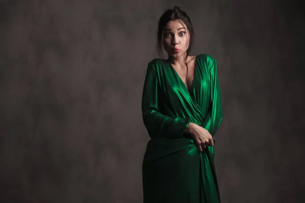 彼女のドレスを保持している灰色の背景の上に立っている間直面して驚いた鴨緑のドレスで面白い女性 — ストック写真
