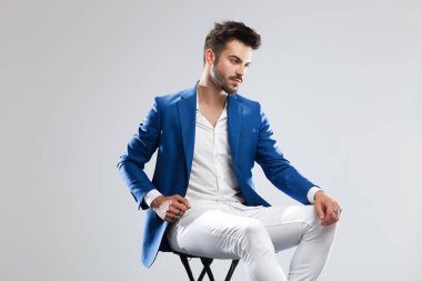 tarafına ışık gri arka plan üzerinde seyir mavi bir takım elbise giyen oturmuş akıllı rahat adam portresi