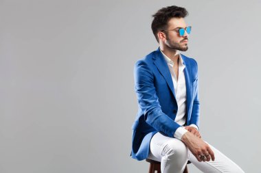 ahşap bir taburede oturan ve üzerinde açık gri renkli tarafına bakarak Genç akıllı casual adam portresi