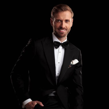 gülümseyen genç adamla eli cebinde smokin siyah arka plan üzerinde oturuyor