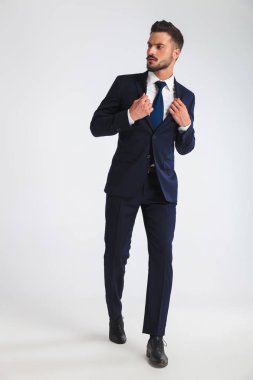 çekici işadamı ise Donanma takım elbise tasmasını tutan ve yan, tam uzunlukta resme bakarak ışık gri arka plan üzerinde adım