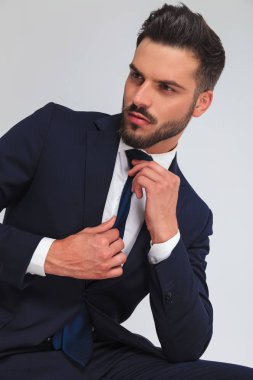 mavi kravatını sabitleme ve tarafına ışık gri arka plan üzerinde seyir oturan işadamı portresi