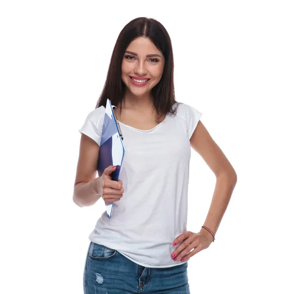 微笑的休闲妇女的肖像手持蓝色剪贴板 同时站在白色背景上 手放在臀部 — 图库照片