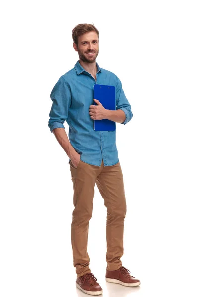白い背景の上のポケットにクリップボードと つの手を保持している笑顔の若いカジュアルな学生 — ストック写真