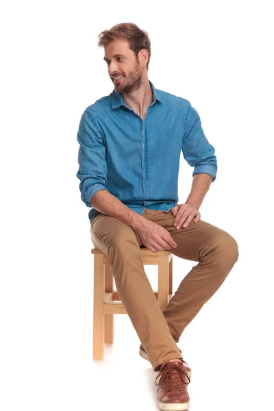 Casual Mann Sitzt Auf Holzstuhl Sieht Zur Seite Auf Weißem — Stockfoto
