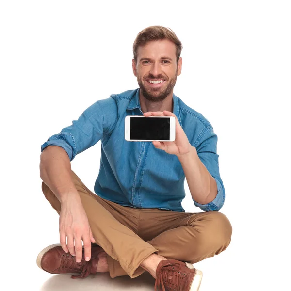 Sedící Usmívající Příležitostné Muž Ukazuje Prázdnou Obrazovku Svého Telefonu Bílém — Stock fotografie