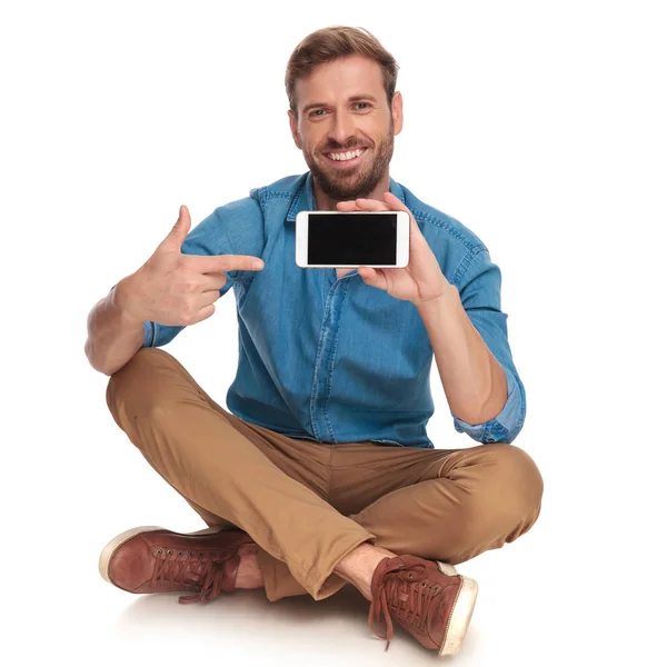 笑坐的休闲男子点手指到他的手机上的白色背景 — 图库照片