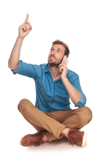 Sentado Casual Homem Fala Telefone Aponta Para Algo Acima Sua — Fotografia de Stock