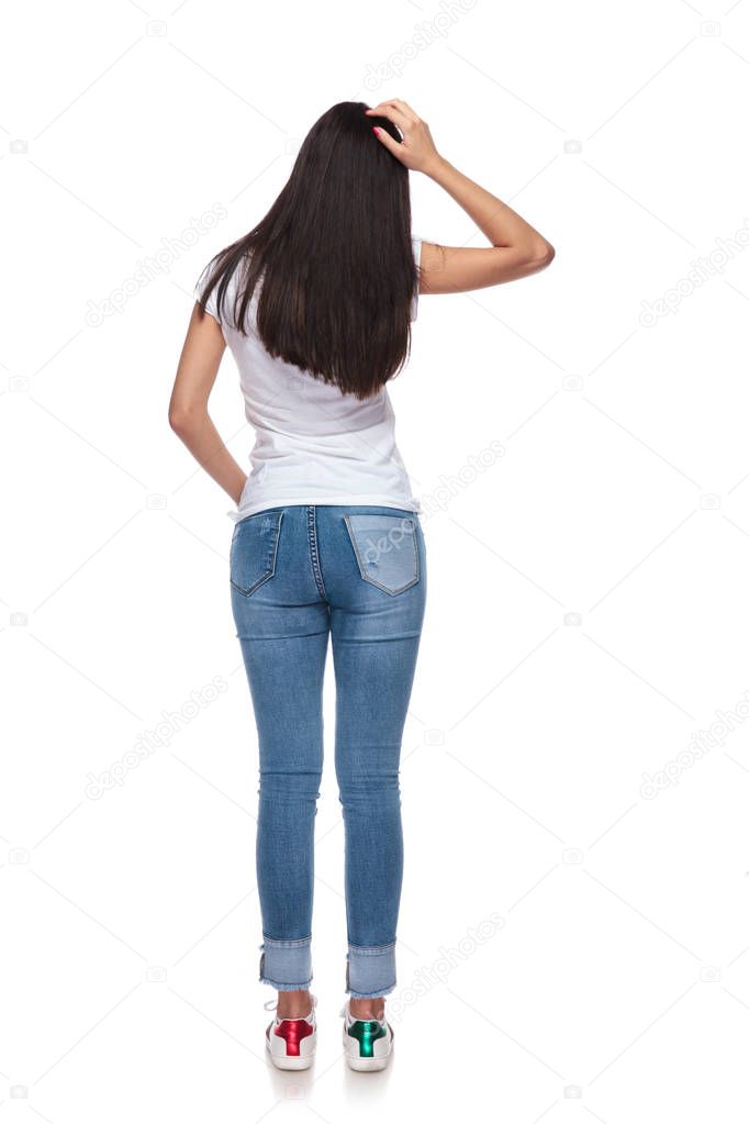 back view of brunette woman scratching her head while standing on white background with a hand in pocket
