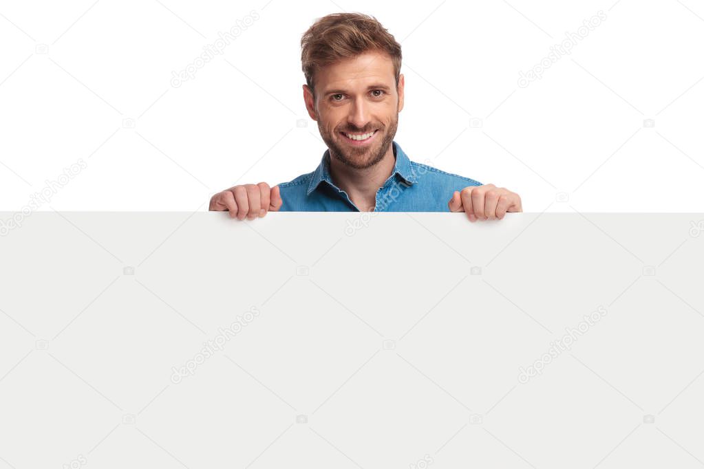 smiling young casual man presenting a blank board on white background