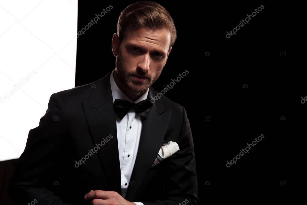 serious elegant man in tuxedo fixing his cufflinks in studio