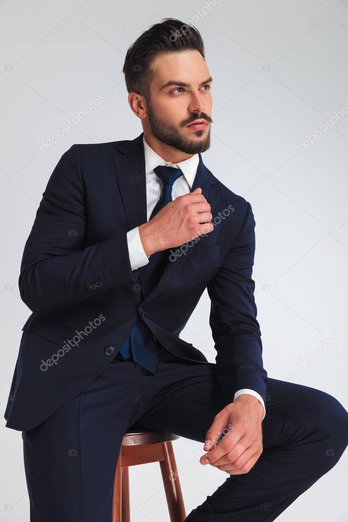 portrait of young businessman relaxing on wooden stool looking up and to side on light grey background