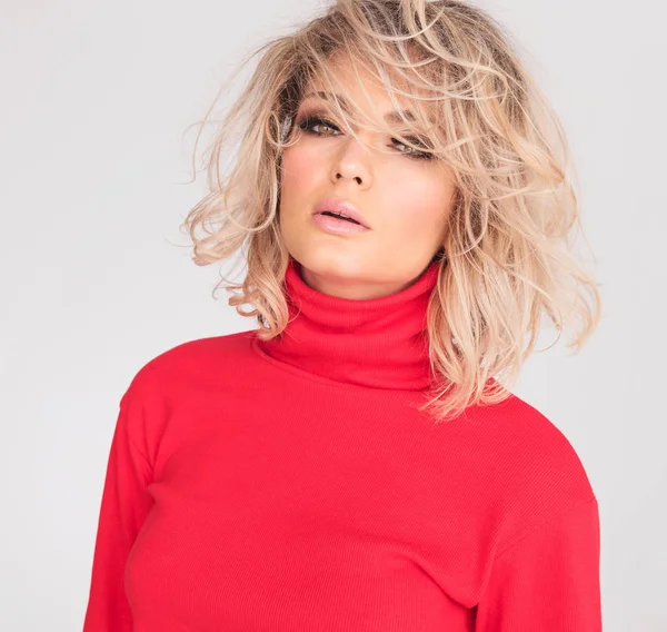 portrait of sensual blonde woman with parted lips standing on white background while wearing a red top