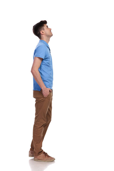 side view of a casual man with hands in pockets looking up at something on white background